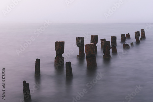 Wooden bridge remains in silky water with sea horizon in the background. Concept of time and tranquility.