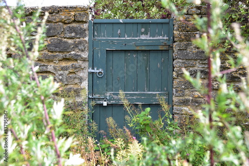 Aged old greed outside door set into a stone wall surrounded by out of focus flora, plants and trees