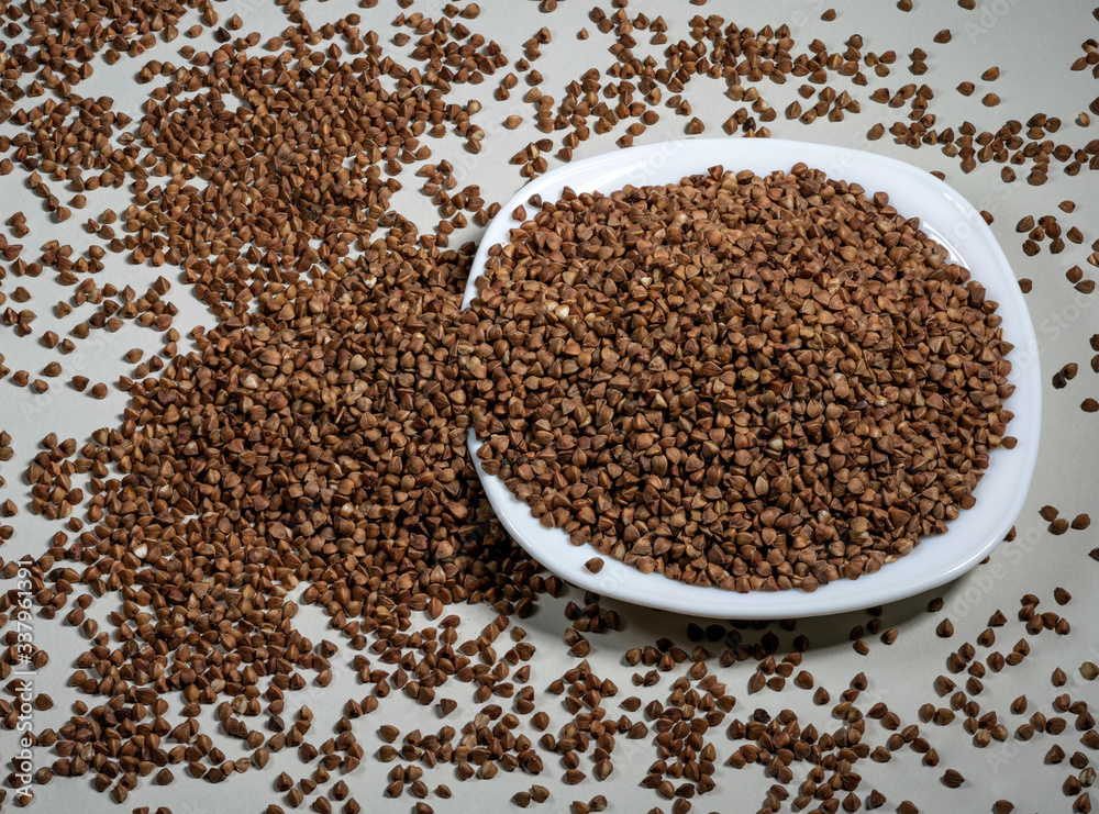 Raw buckwheat in a white plate on a gray background. Ingredient for cooking. View from above. Raw buckwheat in a white plate on a gray background. Ingredient for cooking. View from above.