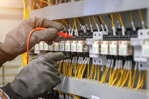 Electrical engineer using digital multimeter to check current voltage at circuit breaker in main distribution board. photo