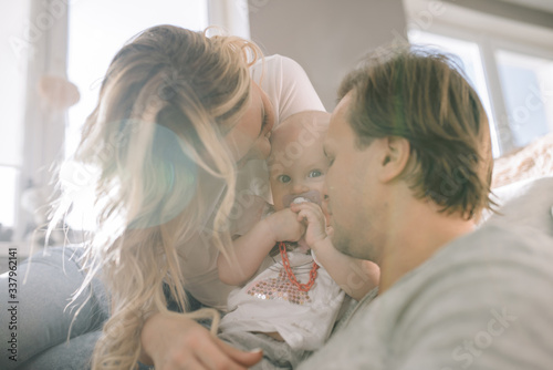 Beautiful family photo. Family sitting on sofa in living room on big window background. The sun is shining from the window. Mom's dad and little baby