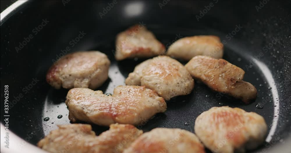Slow motion handheld shot of chicken fillet slices frying on non-stick pan