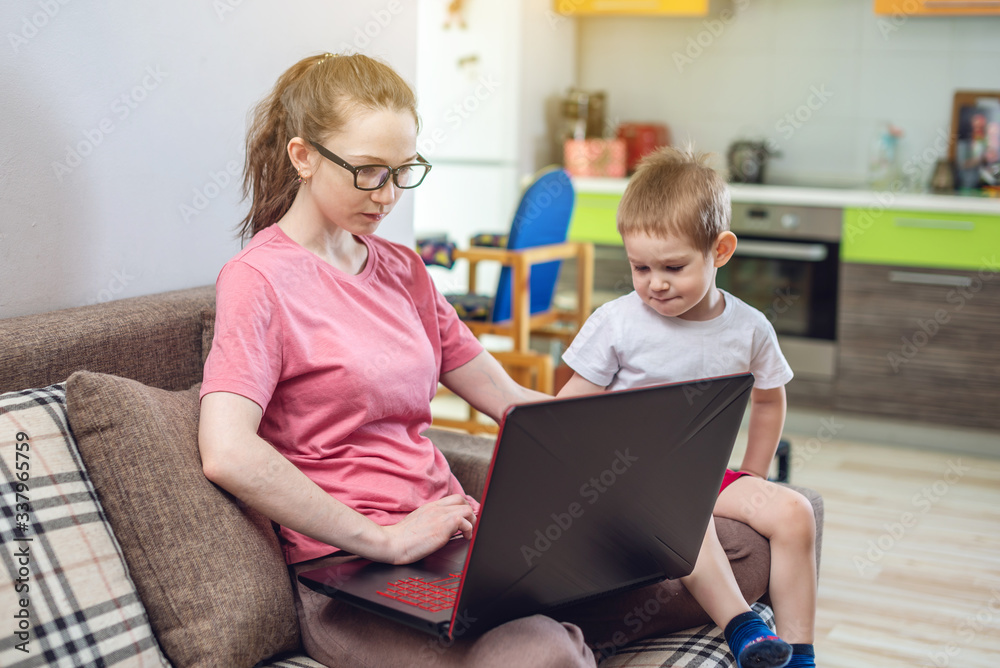Woman with a small child on knees is sitting at a laptop. Remote work and receiving online education of home Woman with a small child on knees is sitting at a laptop. Remote work and receiving online education of home