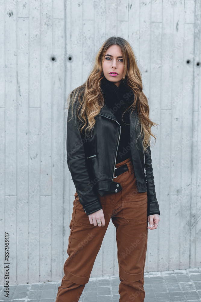 Beautiful independent female lifestyle model  with confident expression wearing autumn collection clothes on a street photshoot with grey wall background