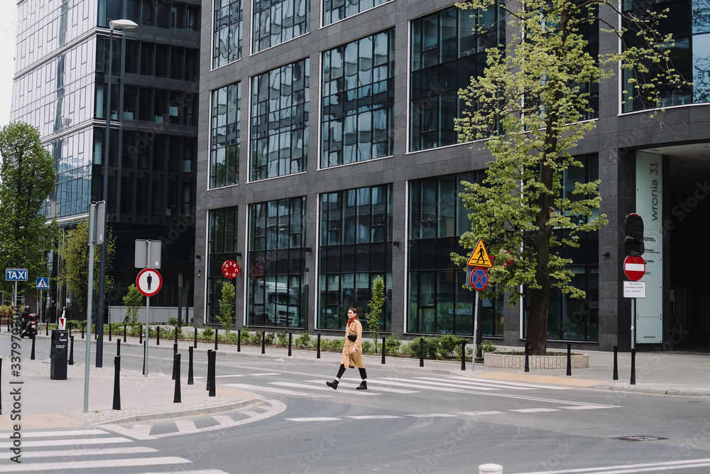 Beautiful young woman in a trench crosses the road near a business center in the city. Beautiful young woman in a trench crosses the road near a business center in the city.