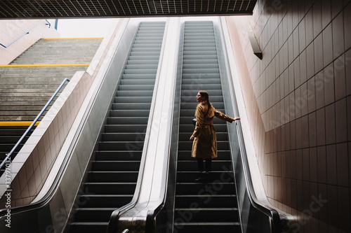Beautiful young woman in trench coat stands on an escalator in the subway. photo