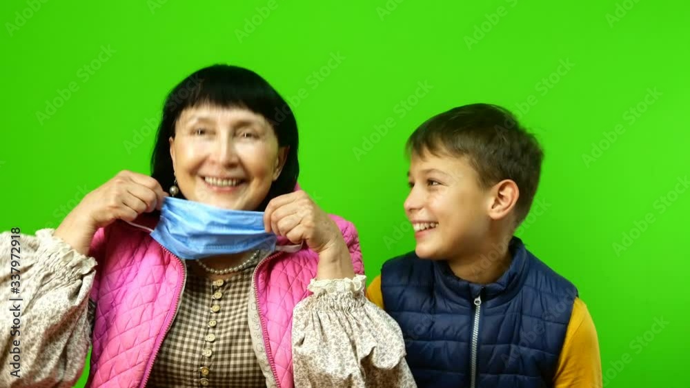 Self-isolation during quarantine. Pastime and entertainment with children in family. Funny grandmother and grandson put on and take off protective medical masks and fool around. Chroma key. Self-isolation during quarantine. Pastime and entertainment with children in family. Funny grandmother and grandson put on and take off protective medical masks and fool around. Chroma key.