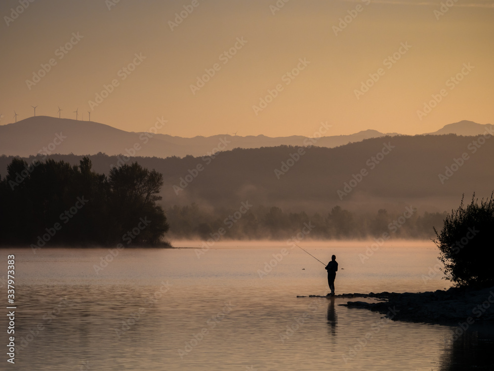 Lonely fisherman angling at a lake in the early morning just after sunrise, Ullibarri-Gamboa Reservoir, Alava, Basque Country, Spain Lonely fisherman angling at a lake in the early morning just after sunrise, Ullibarri-Gamboa Reservoir, Alava, Basque Country, Spain