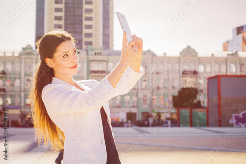 Beautiful brunette business woman in white suit working on a tablet in her hands outdoors. copy space