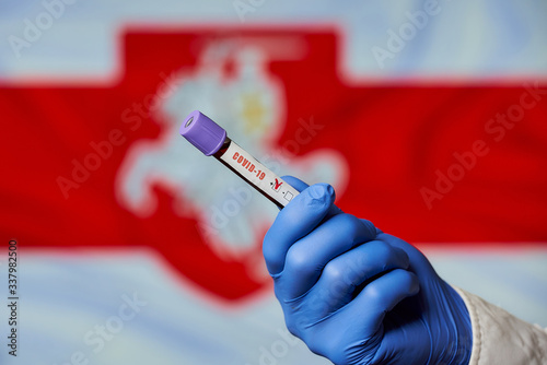 A hand of an infectious disease physician in a blue disposable medical glove holding a positive coronavirus (COVID-19) blood test against the White-Red-White flag with the emblem Pahonia of Belarus. photo