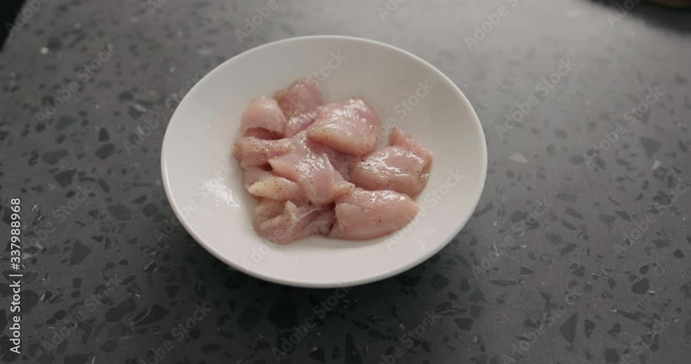 Slow motion raw chicken fillet marintaing with spices in white bowl on concrete countertop Slow motion raw chicken fillet marintaing with spices in white bowl on concrete countertop