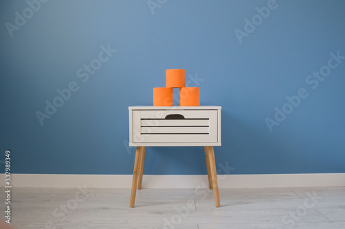 Rolls of luxury creative orange toilet paper standing on white nightstand on blue wall background with copy space for your creative design. Creative concept
