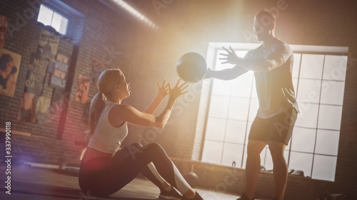 Young Girl Exercises with Personal Trainer, Doing Sit-ups with Medicine Ball, Throwing Pass Back and Forth. Strong Couple Workout. Exercising Strength, Cardio and Power. Shot with Warm Sun Flare. photo