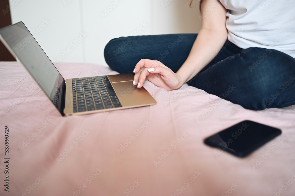 Naklejka premium Young european woman in face medicine mask working on a laptop and phone in bed during coronavirus isolation home quarantine. Covid-19 pandemic Corona virus. Distance online work from home concept.