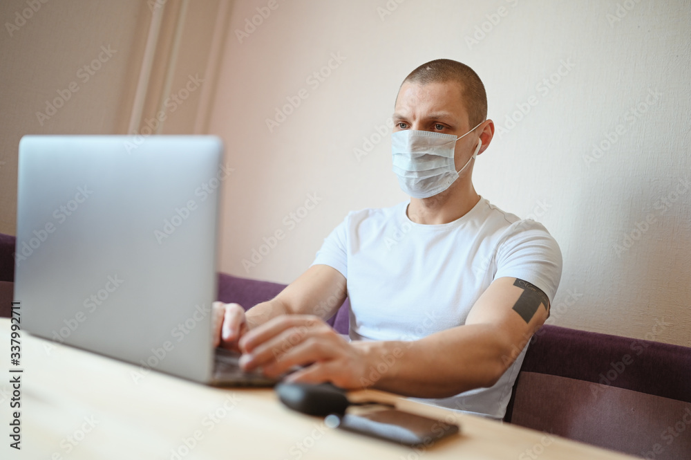 Young european man in face protective medicine mask working on a laptop during coronavirus isolation home quarantine. Covid-19 pandemic Corona virus. Distance online work from home concept. Young european man in face protective medicine mask working on a laptop during coronavirus isolation home quarantine. Covid-19 pandemic Corona virus. Distance online work from home concept.
