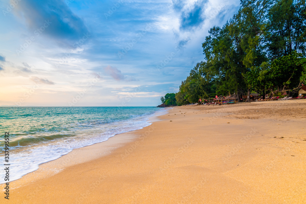 View of tropical beach at Koh Lanta island, Thailand. Bar on the beach are prepared for tourist during beautiful sunset. Soft light, vibrant colors. Sky with clouds above tranquil sea.