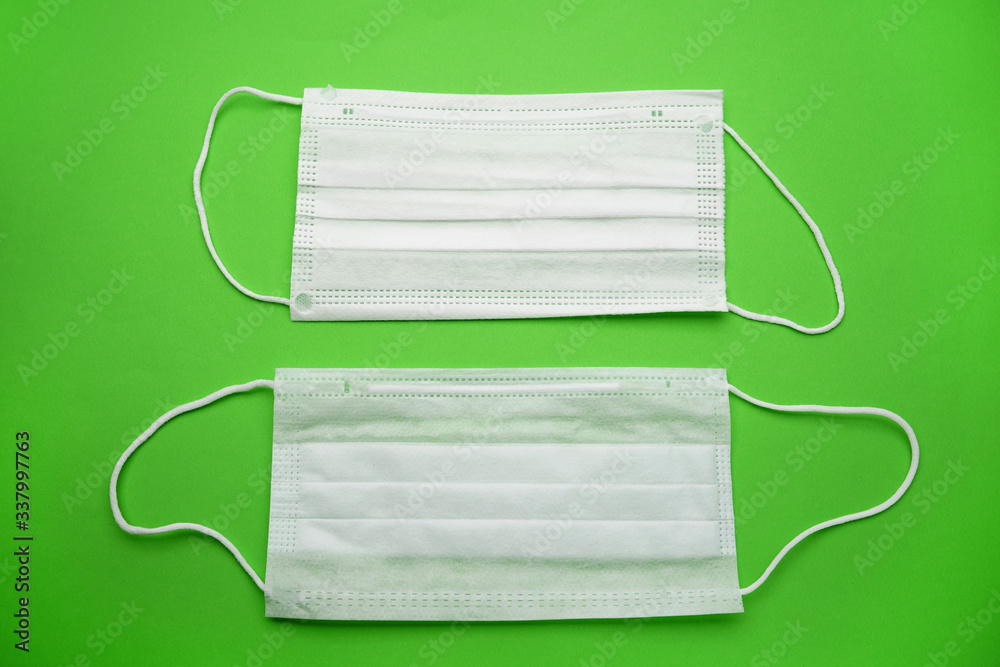 Two medical face masks isolated on a green background.