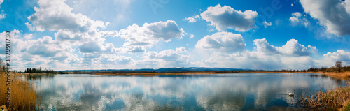 Panoramic landscape from the lake shore with colorful clouds in the spring sun.