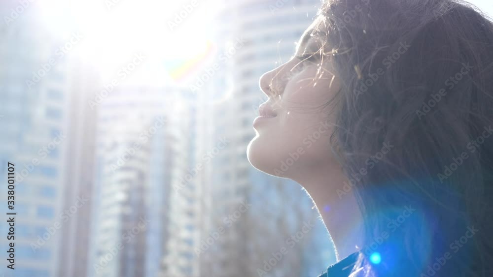 Beautiful satisfied urban girl takes off mask outdoors. Calm smiling young woman feels tranquility, deep enjoyment sunbeams, air breeze by day closeup. Carefree recreation on clean streets of big city