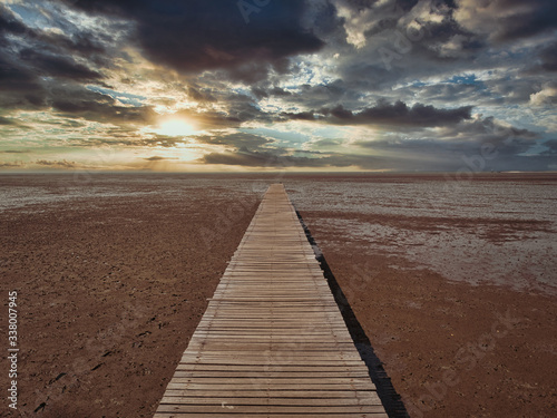 Fototapeta Naklejka Na Ścianę i Meble -  The wooden bridge that extends into the sea as a viewing point during the low tide during the sunset time in the beautiful atmosphere.