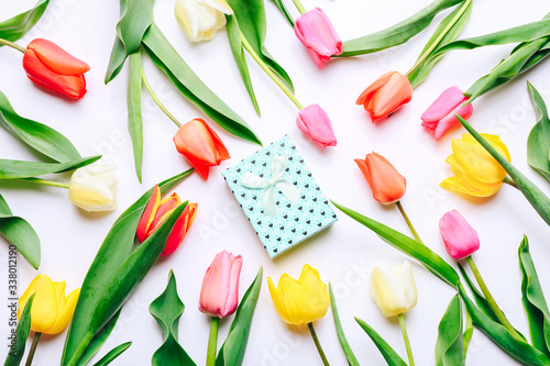 Beautiful tulips lying around gift box on white background, top view