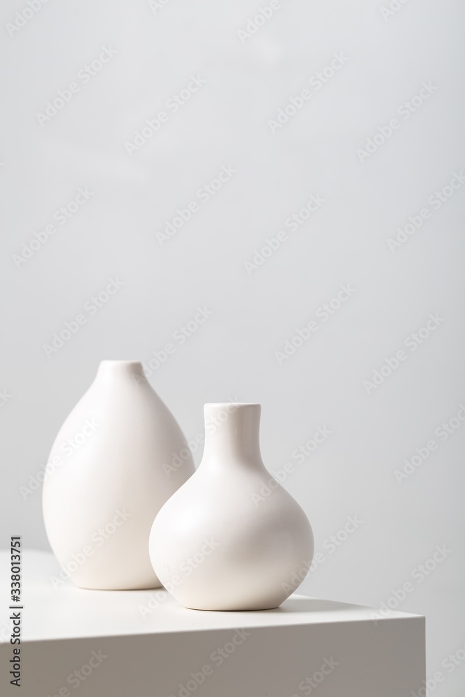 Closeup of two white clay vases on the table under the lights against a white background - obrazy, fototapety, plakaty 