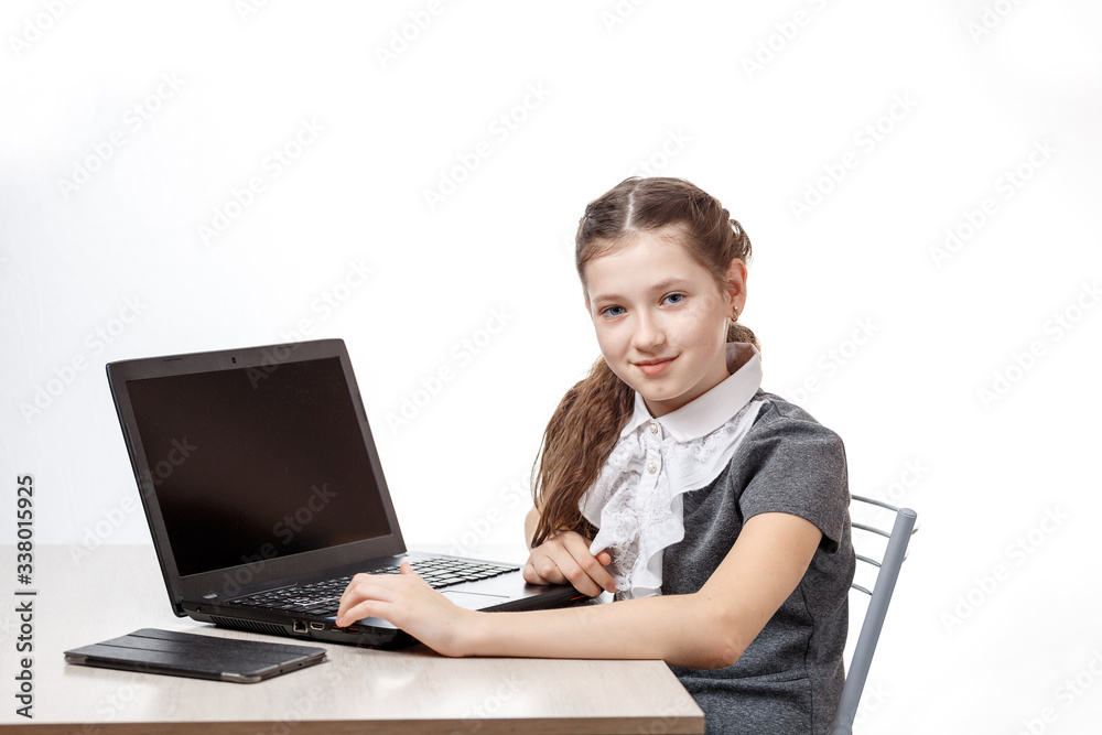 Cute schoolgirl sitting at a laptop on a white background