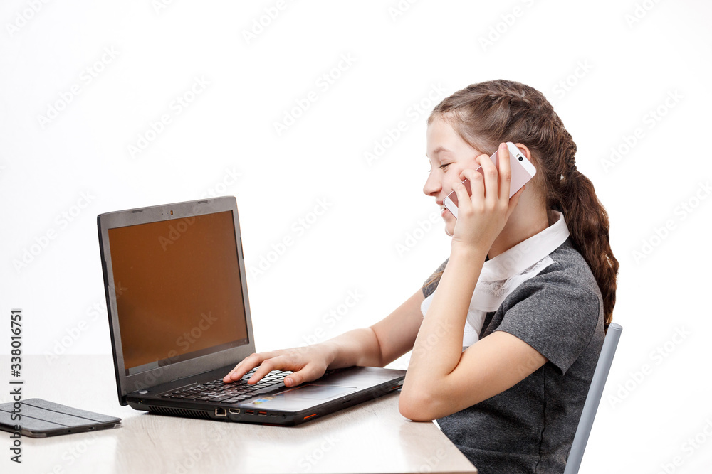 Cute schoolgirl sitting at a laptop and talking on the phone on a white background Cute schoolgirl sitting at a laptop and talking on the phone on a white background