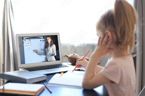 Distance learning. Cheerful little girl using laptop computer studying through online e-learning system.