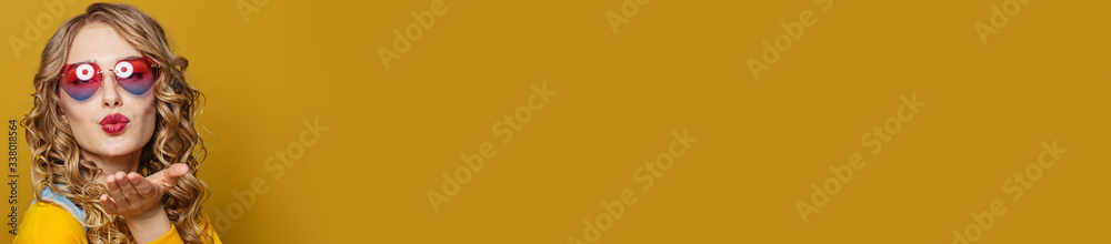 Lovely woman in heart sunglasses blowing kiss on bright yellow background. Positive emotion Lovely woman in heart sunglasses blowing kiss on bright yellow background. Positive emotion