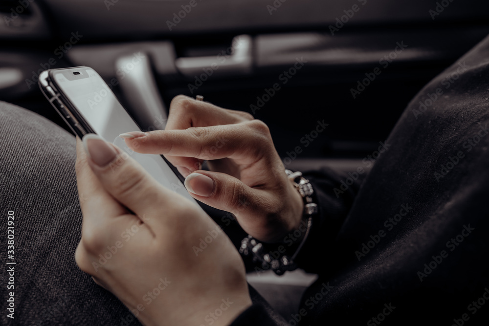 Woman using mobile phone over dark background in car. Close up beautiful hands holding smartphone. Female using technology.