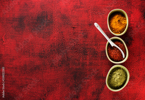 Fototapeta Naklejka Na Ścianę i Meble -  Indian spices seasoning spicy in bowls on a red background and copy space for text, top view. powder chili, turmeric curry and cardamom