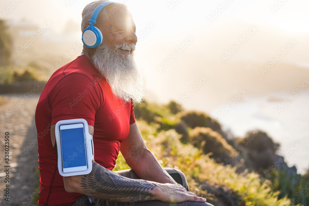 Senior fit man outdoor at sunset after workout session - Mature athlete training outside while listening playlist music with bluetooth headphones - Sport and joyful elderly lifestyle concept