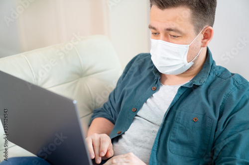 male freelancer in medical mask working on couch