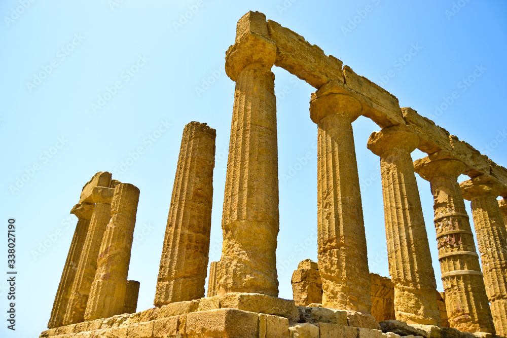 Golden ruins of an ancient Greek temple with broken columns and missing pieces under a bright sky in the Italian isle of Sicily 