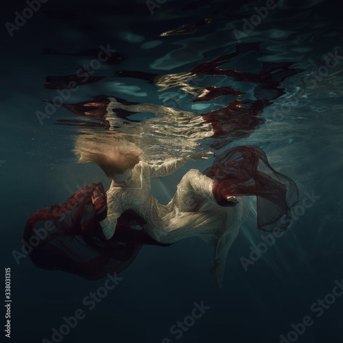 A woman in a long sequined dress swims underwater