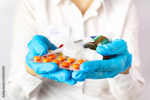 Close-up of a female doctor in blue medical gloves and a uniform holding pills and bottles with drops on her hands stretched forward. Medicine, vitamins and antibiotics to treat health and viruses.