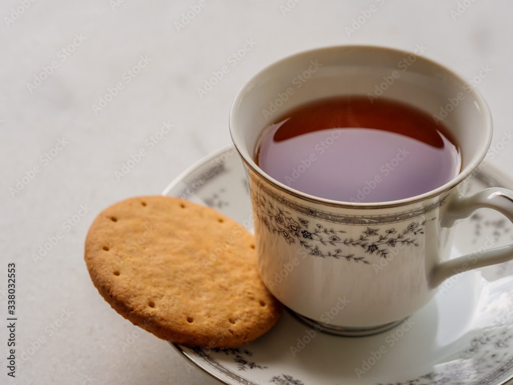Close up of English tea in a porcelain china cup with a digestive biscuit Close up of English tea in a porcelain china cup with a digestive biscuit