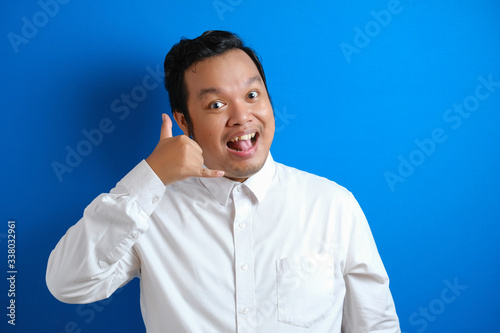 Young Asian businessman in formal white shirt smiling at camera and shows call me telephone sign