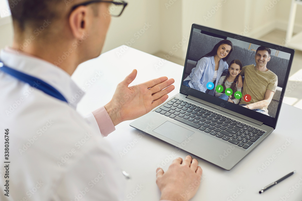Family doctor online. Male doctor speaks with patients by family using laptop sitting behind straw in clinic office. Family doctor online. Male doctor speaks with patients by family using laptop sitting behind straw in clinic office.