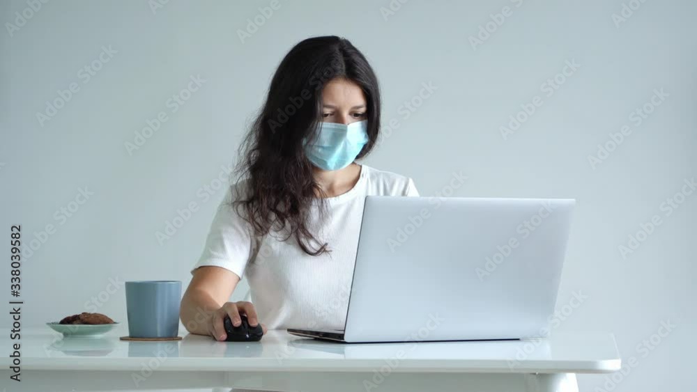 The girl works from home during quarantine. Corona virus pandemic. A girl in a surgical mask works on a laptop and drinks coffee. Distant work The girl works from home during quarantine. Corona virus pandemic. A girl in a surgical mask works on a laptop and drinks coffee. Distant work