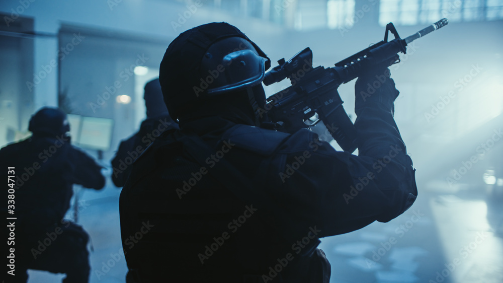 Portrait of Masked Armed SWAT Police Officer Storming Dark Seized Office Building with Desks and Computers. Soldiers with Rifles and Flashlights Move Forward and Cover Surroundings. Portrait of Masked Armed SWAT Police Officer Storming Dark Seized Office Building with Desks and Computers. Soldiers with Rifles and Flashlights Move Forward and Cover Surroundings.