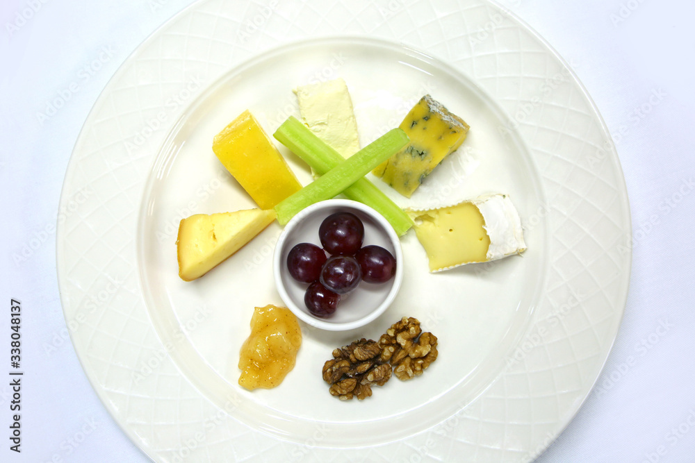 A selection of cheeses with grapes, chutney, celery & walnuts all prepared to serve as a cheese plate, on a white table cloth. A selection of cheeses with grapes, chutney, celery & walnuts all prepared to serve as a cheese plate, on a white table cloth.