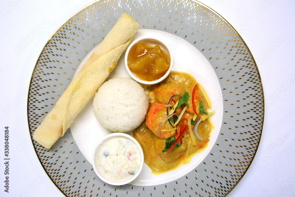 An Indian dinner ready to serve with chicken tikka masala, rice, chutney, raita, and a chapati bread, on a grey ornate plate & white table cloth. An Indian dinner ready to serve with chicken tikka masala, rice, chutney, raita, and a chapati bread, on a grey ornate plate & white table cloth.
