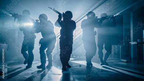 Masked Team of Armed SWAT Police Officers Move in a Hall of a Dark Seized Office Building with Desks and Computers. Soldiers with Rifles and Flashlights Surveil and Cover Surroundings.