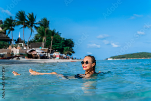 An attractive young girl is bathing in the calm sea on the beach in clear turquoise sea water. Portrait of a young girl in the water on a sandy beach.