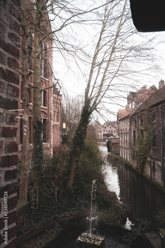 Narrow water cannal in Bruges with a reflection, picture taken from restaurant. Fountain in foreground