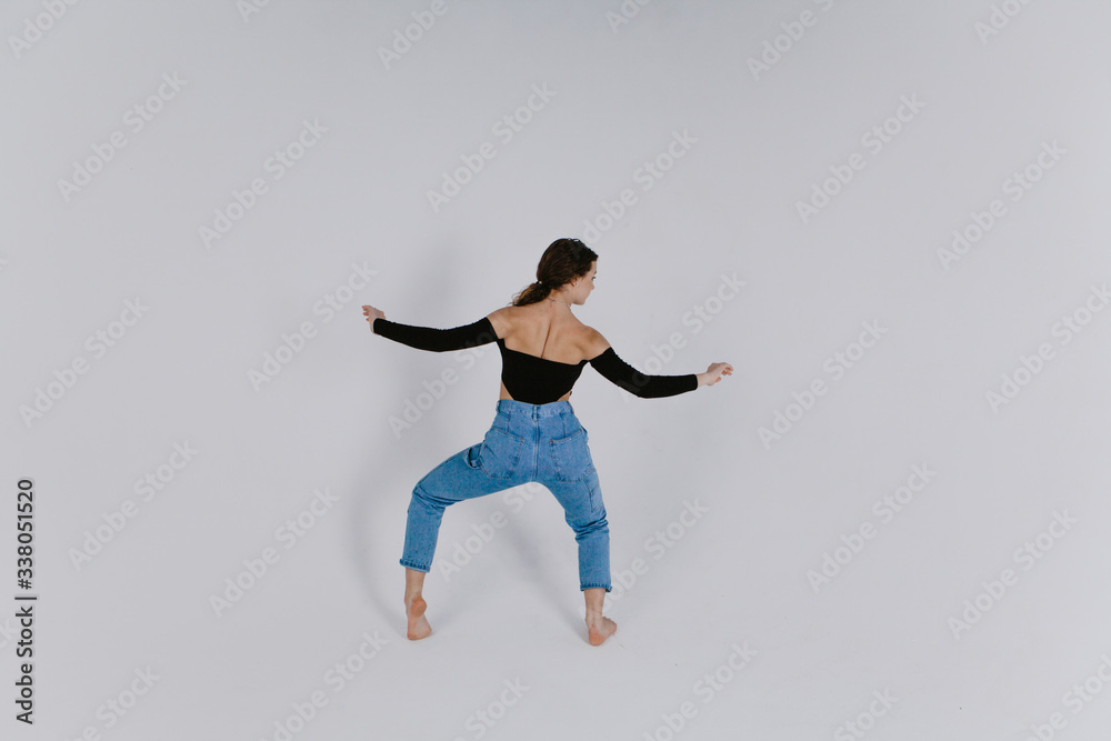 Fototapeta premium Stylish beautiful dancer wearing black leotard with open shoulders and blue jeans dancing on the white backgroud