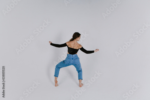 Stylish beautiful dancer wearing black leotard with open shoulders and blue jeans dancing on the white backgroud