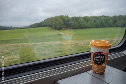 Coffee in big cup on steel table in train with blurred view of fresh green trees at rural area with cloudy sky background with copy space